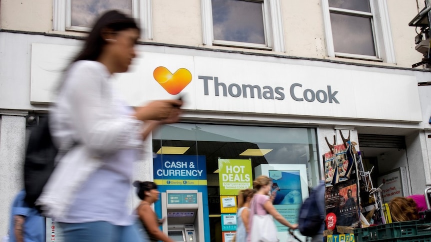 Pedestrians walk past an office with Thomas Cook branding