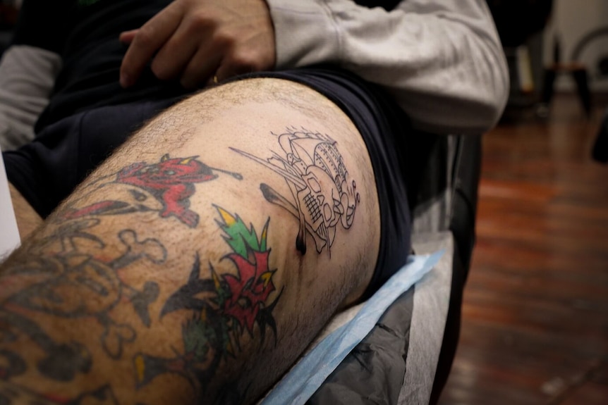 A stencil of a skull and ship drawn on a man's leg. 