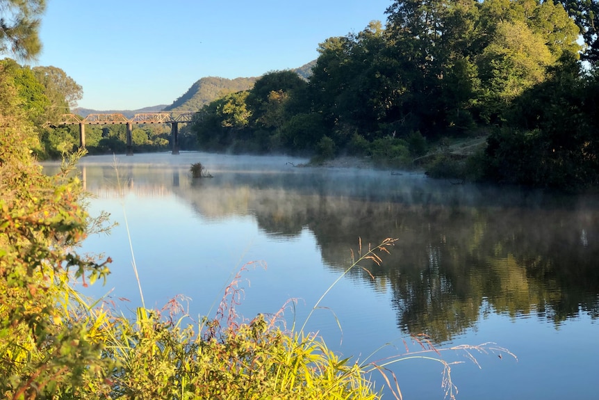 A beautiful stretch of river with a rusty rail bridge and mountains in the distance.