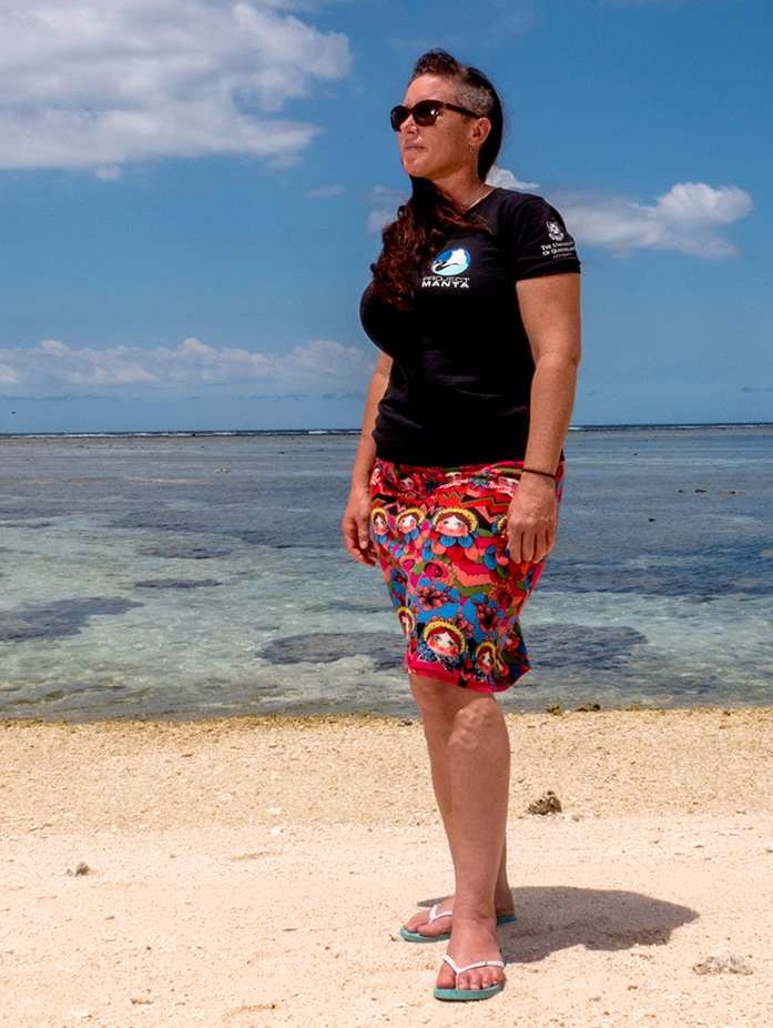 A woman stands on a coral beach.