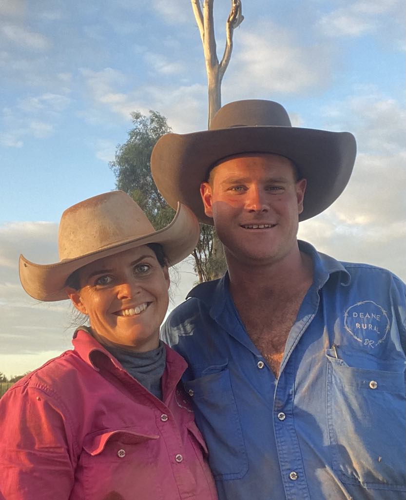 A young man and woman smile at the camera wearing button up work shirts and hats