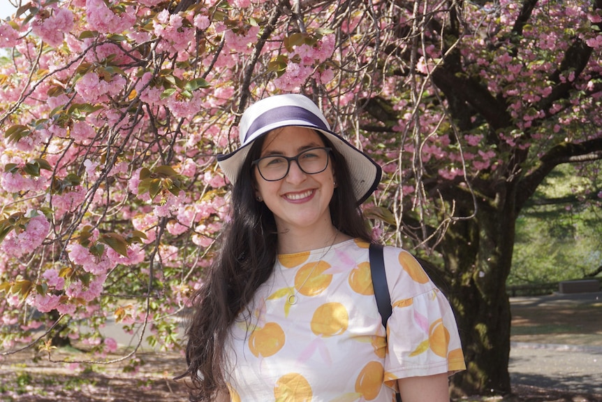 Natalia Faranda smiling at camera with hat on in front of a flowering tree