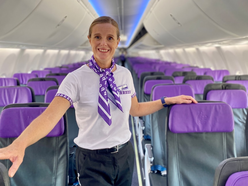 A flight attendant posing inside a plane.