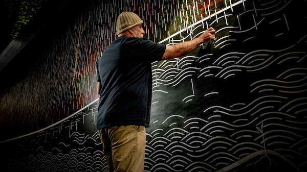 Shane Smithers, in a beanie, paints intricate white lines on a large mural