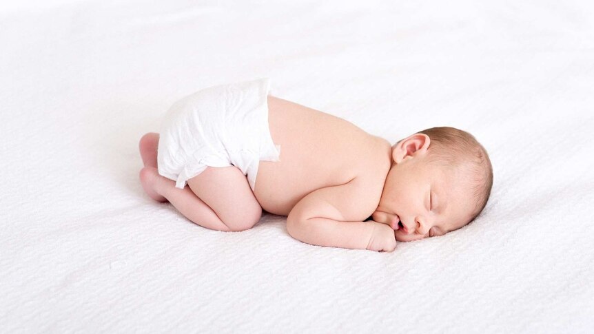 a newborn baby wearing just a nappy sleeps on a sheet