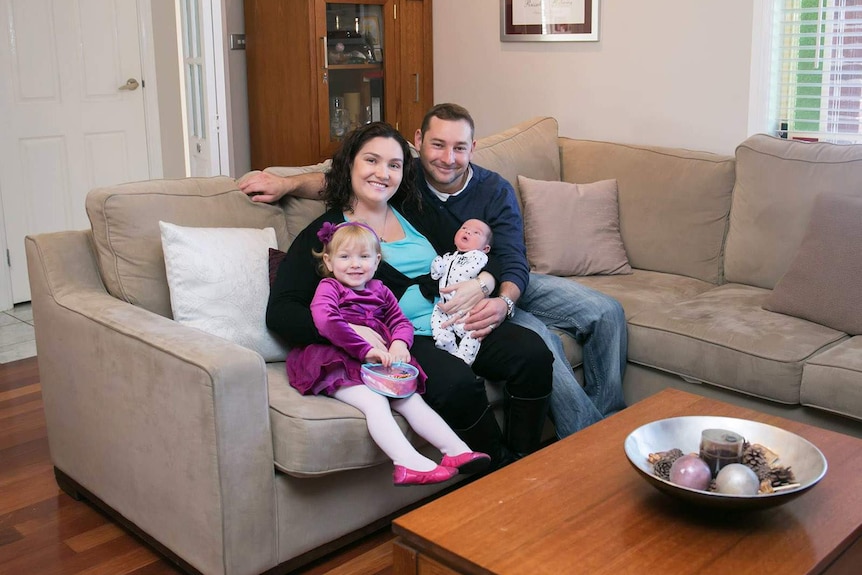 Bec Tucker, her partner and two children sit on a lounge at home.