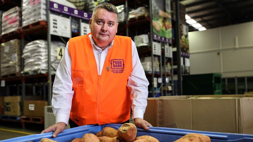 Michael Rose, CEO Foodbank Queensland berdiri di dekat tumpukan ubi manis di gudang makanan di Brisbane.