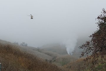 Smoking wreck in the Malibu hills, with another helicopter flying above.