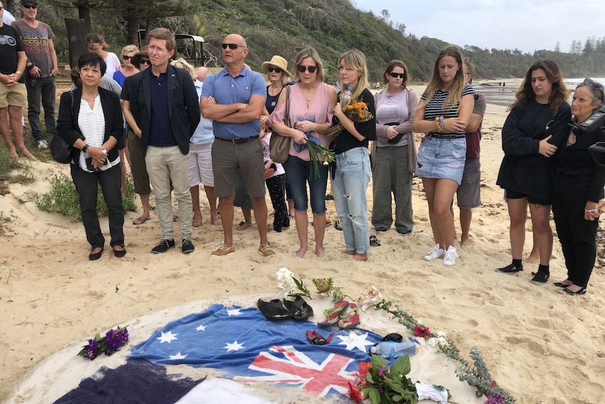 A group of people standing on a beach in front of an Australian and French flag.