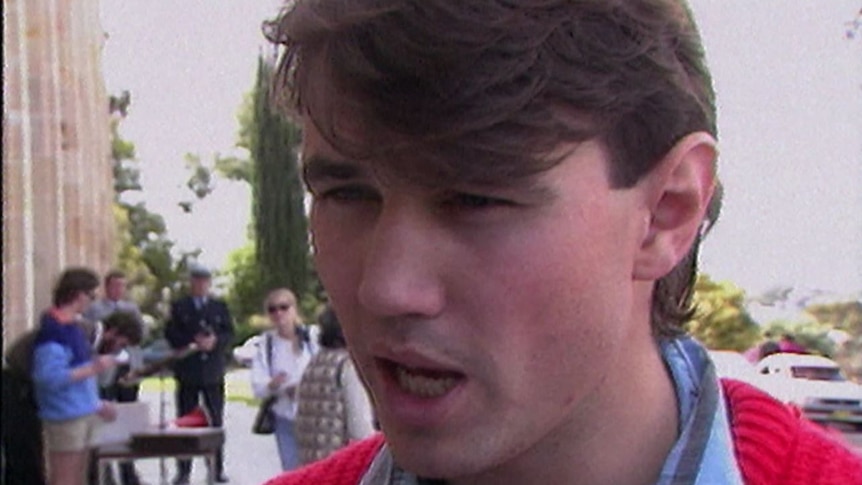 A young man wearing a red jumper with a blue shirt collar sticking out.