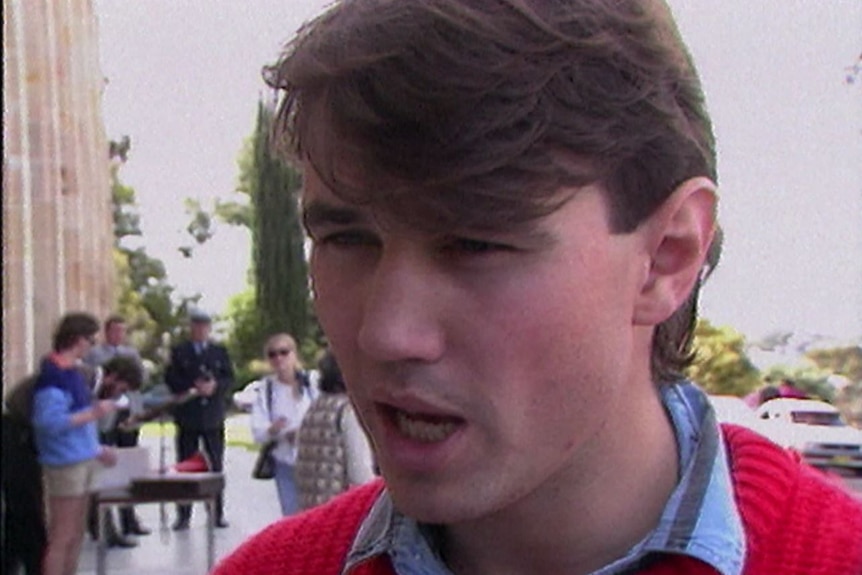 A young man wearing a red jumper with a blue shirt collar sticking out.