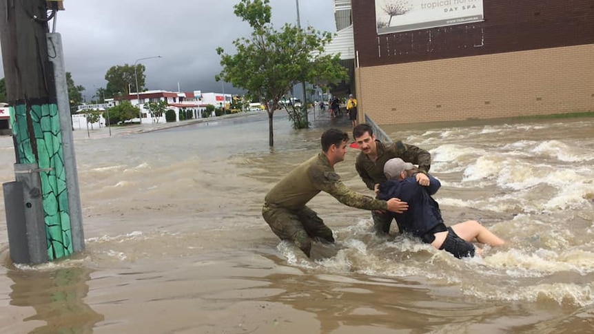 Two personnel help a man laying in flood waters in Townsville.