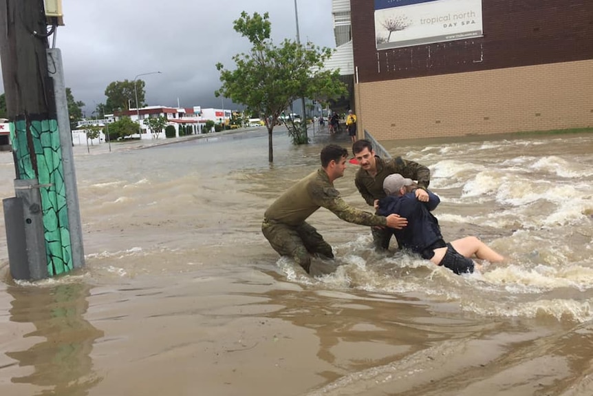 two men dressed in cargo help a man laying in flood waters