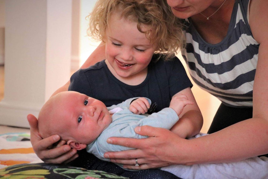 Rosie Slatterly holding her new baby brother George as he looks at the camera.