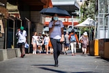 A woman wearing a face mask and holding an umbrella walks away from Perth train station.