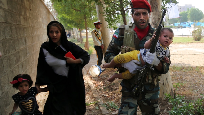 Iranian army soldier carries child away from a shooting scene alongside and woman and small girl