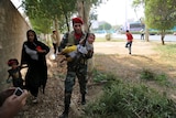 Iranian army soldier carries child away from a shooting scene alongside and woman and small girl