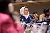 Nayebi sits at a UN roundtable making a point by holding her left hand in a pincer-like pose in front of a mic.