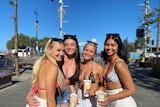 Four young women in beach gear stand in the sun, smiling.