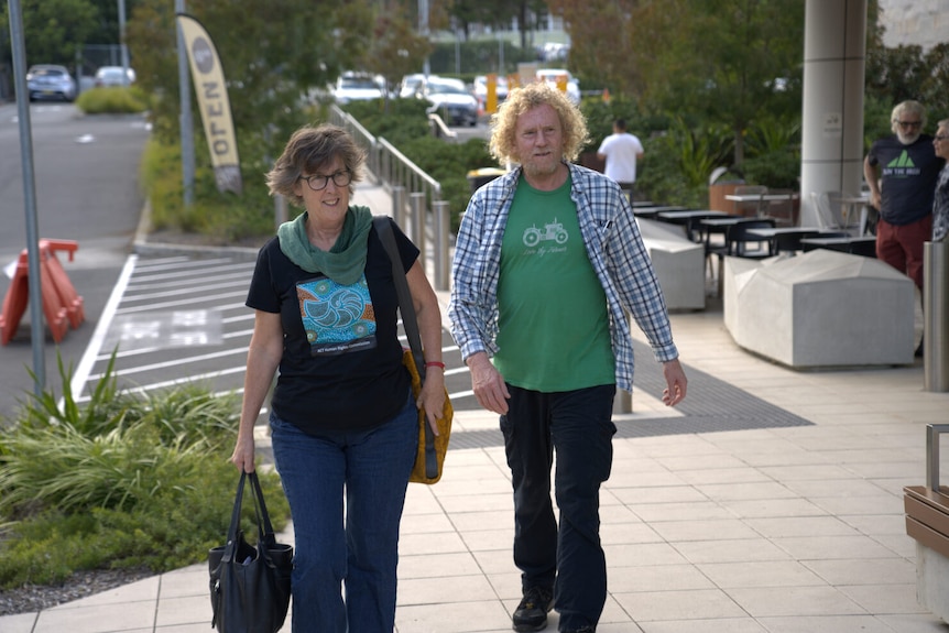 A woman holding two bags and a man walk along a footpath.