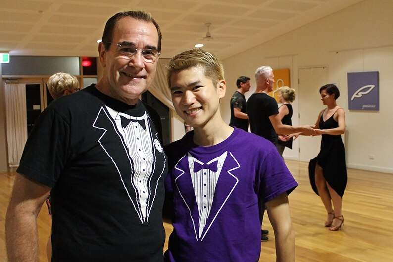 Two men in matching tuxedo shirts standing in a busy dance hall.