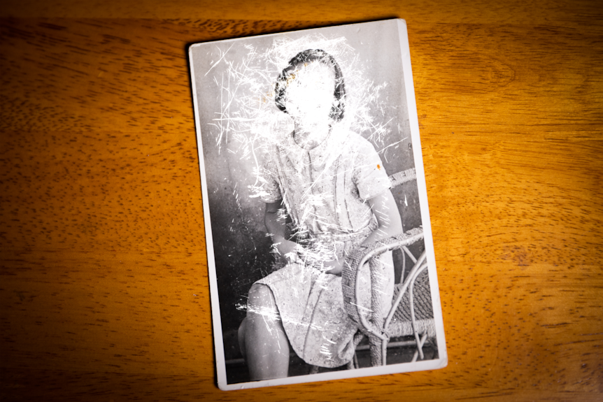 An old, black and white photo of a girl which has been scratched to conceal her face.