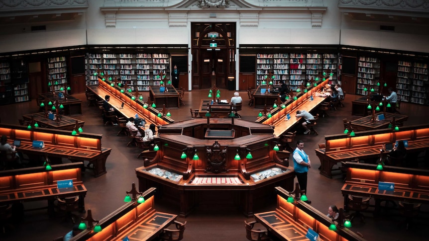 A high-angled view of an ornate orthagonal library floor, with green lamps illuminating desks radiating from the centre.