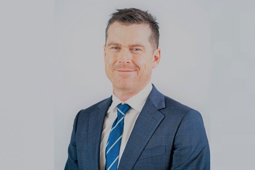 Head of AFL Victoria Ben Kavenagh looks at the camera in a suit and tie in front of a blank background.