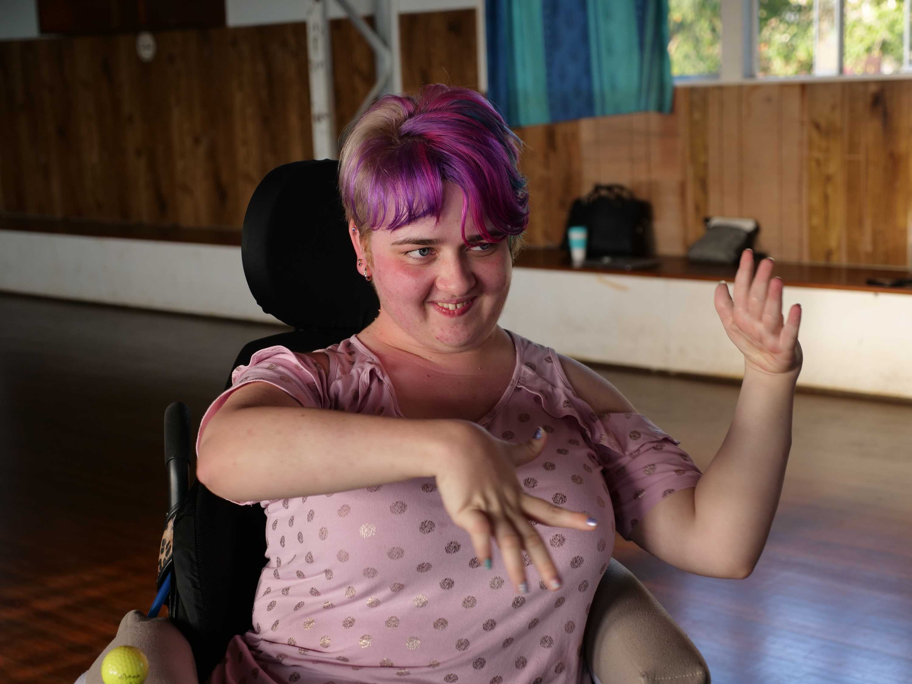 A young woman with pink hair in a wheelchair dancing.