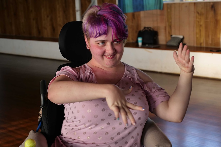 A young woman with pink hair in a wheelchair dancing.