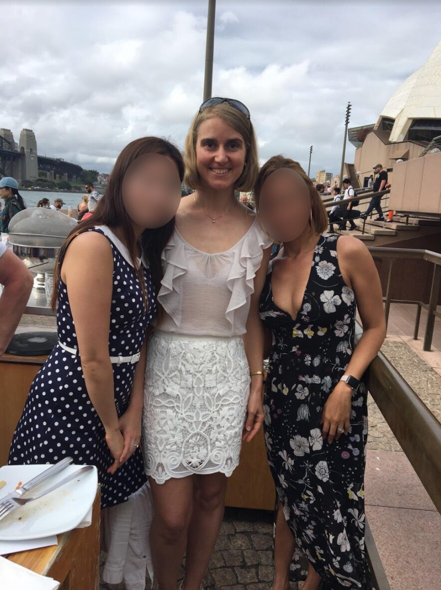 Woman with short her stands between two other women, whose faces are blurred.