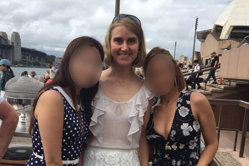 Woman with short her stands between two other women, whose faces are blurred.