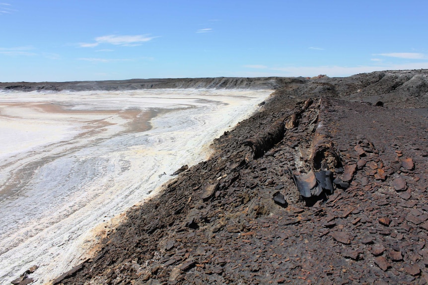 A close shot of vast black mine tailings. A highly saline area has formed to the left.