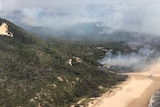 Plumes of smoke heads into the air, covering parts of Fraser Island, including the beach.