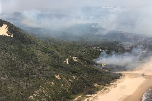 Plumes of smoke heads into the air, covering parts of Fraser Island, including the beach.