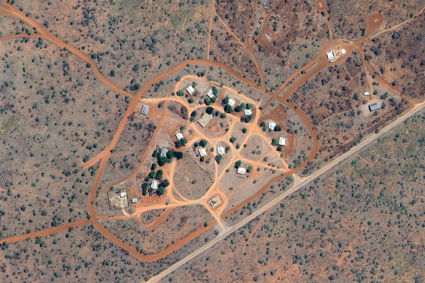 A satellite image of a dozen houses and red dirt roads, surrounded by desert shrub