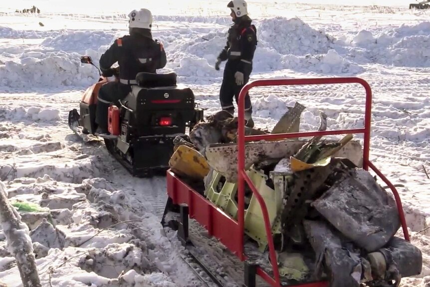 Emergency workers carry the wreckage of a plane on a snowmobile.