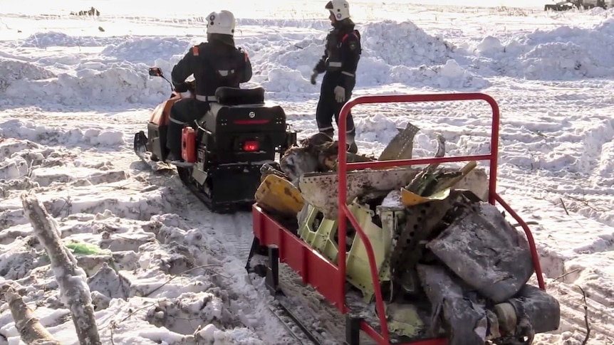 Emergency workers carry the wreckage of a plane on a snowmobile.