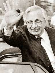 Black and white photo of Mafia leader Licio Gelli waving as he gets into a car.