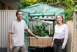 Alexis and Marion stand smiling in front of their diy aquaponics system set up in their courtyard 