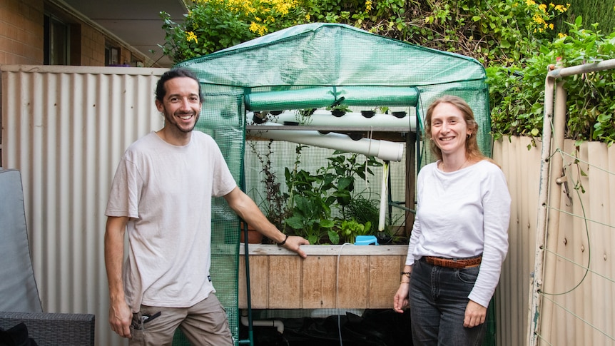 Alexis and Marion stand smiling in front of their diy aquaponics system set up in their courtyard 