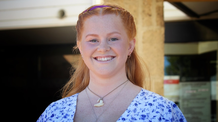 A young, ginger-haired woman with a big smile, wearing a dress outside a courthouse.