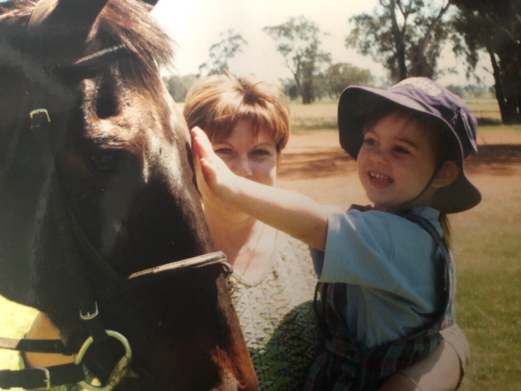 A mother holds up a small girl so she can pat a horse.