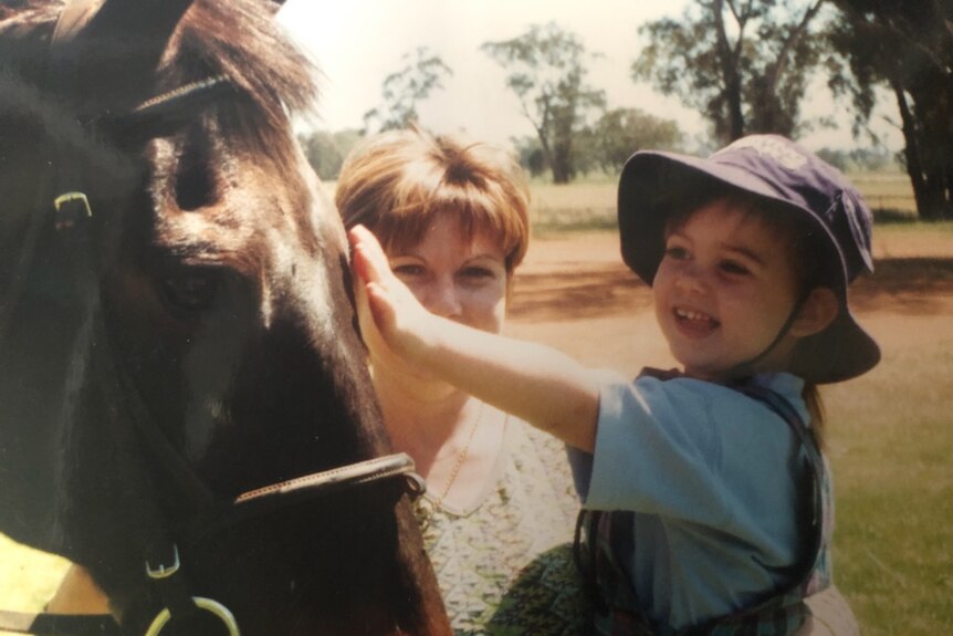 A mother holds up a small girl so she can pat a horse.