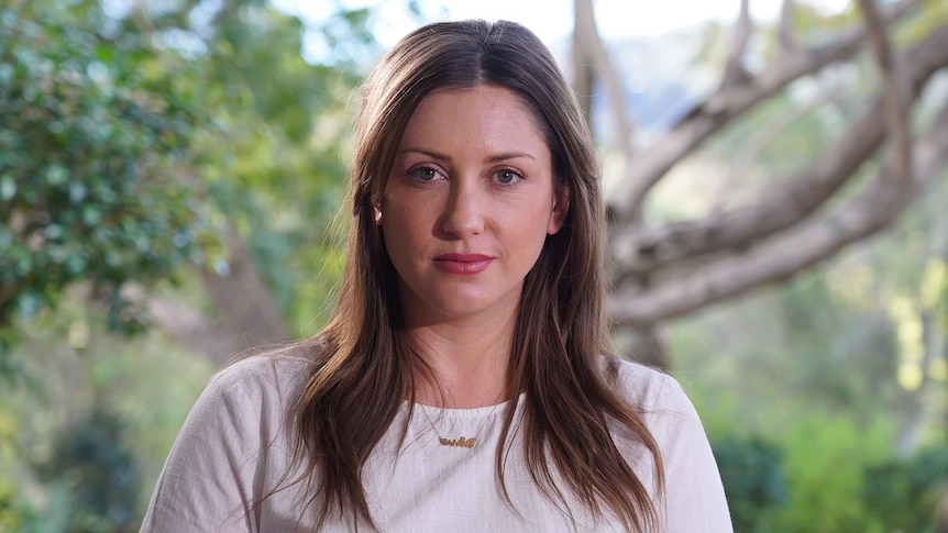 A woman with long brown hair stares sternly down the barrel of the camera. 