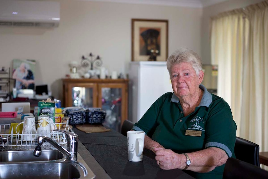 An older woman sits at a breakfast bar in her home with a cup of coffee.