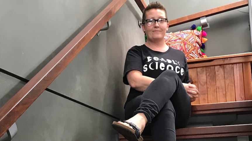 A woman wearing black jeans and tshirt sits on a staircase.