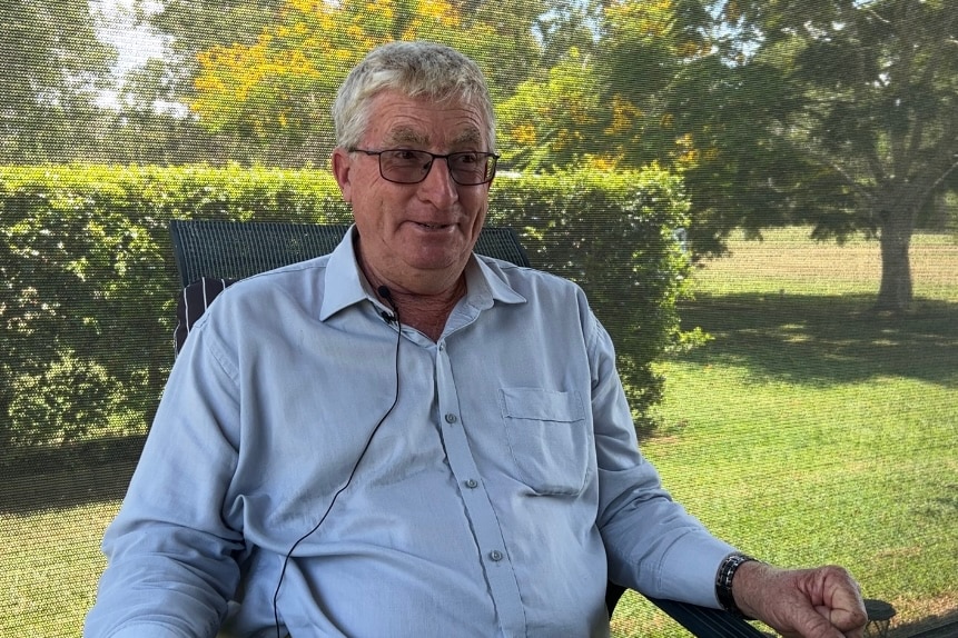 A man in a blue shirt and glasses smiles while seated