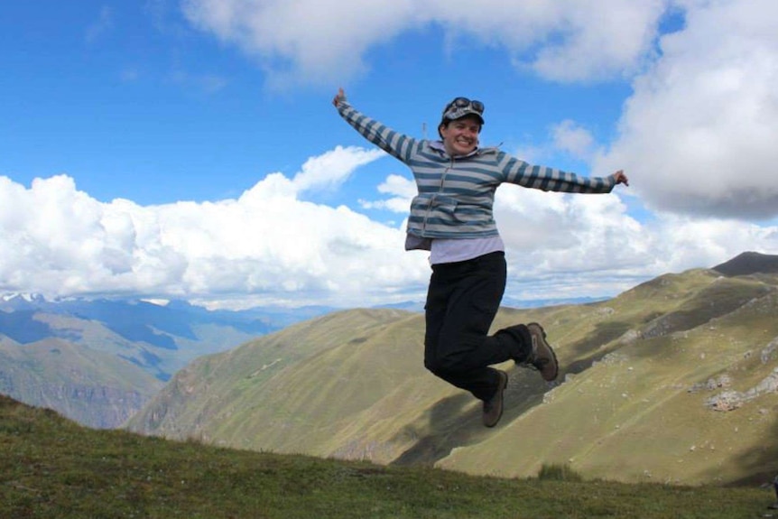 Erin Davidson is mid-air with her arms spread out after jumping off the ground while in the midst of the mountains in Peru.