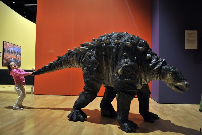 Three-year-old Lauren pulls on a dinosaur's tail at a museum.